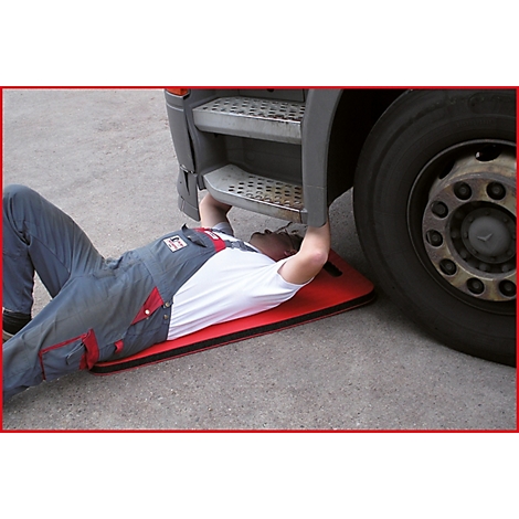 Ein Mann liegt unter einem LKW, auf einer roten Matte. Er arbeitet an der Unterseite des Fahrzeugs.